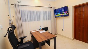 Ett hotellrum med ett träbord, två svarta stolar, en tv som är monterad på väggen och en trädörr.