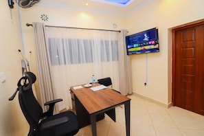 Habitación de hotel con una mesa de madera, dos sillas negras, un televisor montado en la pared y una puerta de madera.