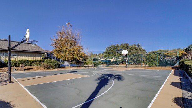 An outdoor basketball court with a clear sky, a tennis court building, and a tree in the background. - Sunset Rentals | Island Club 101 (Hilton Head Island)