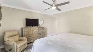 A bedroom with a bed, a recliner, a dresser, a ceiling fan, and a television. - Sunset Rentals | Island Club 101 (Hilton Head Island)