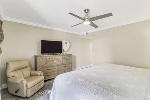 Ein Schlafzimmer mit einem Bett, einem Liegestuhl, einem Schminktisch, einem Deckenventilator und einem Fernseher.