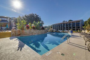 Ein Swimmingpool mit einer Steinmauer und einer Metallleiter, umgeben von Liegestühlen und Sonnenschirmen.