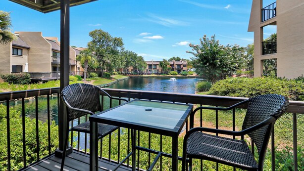 Een balkon met tafel en stoelen met uitzicht op een waterpartij en gebouwen.