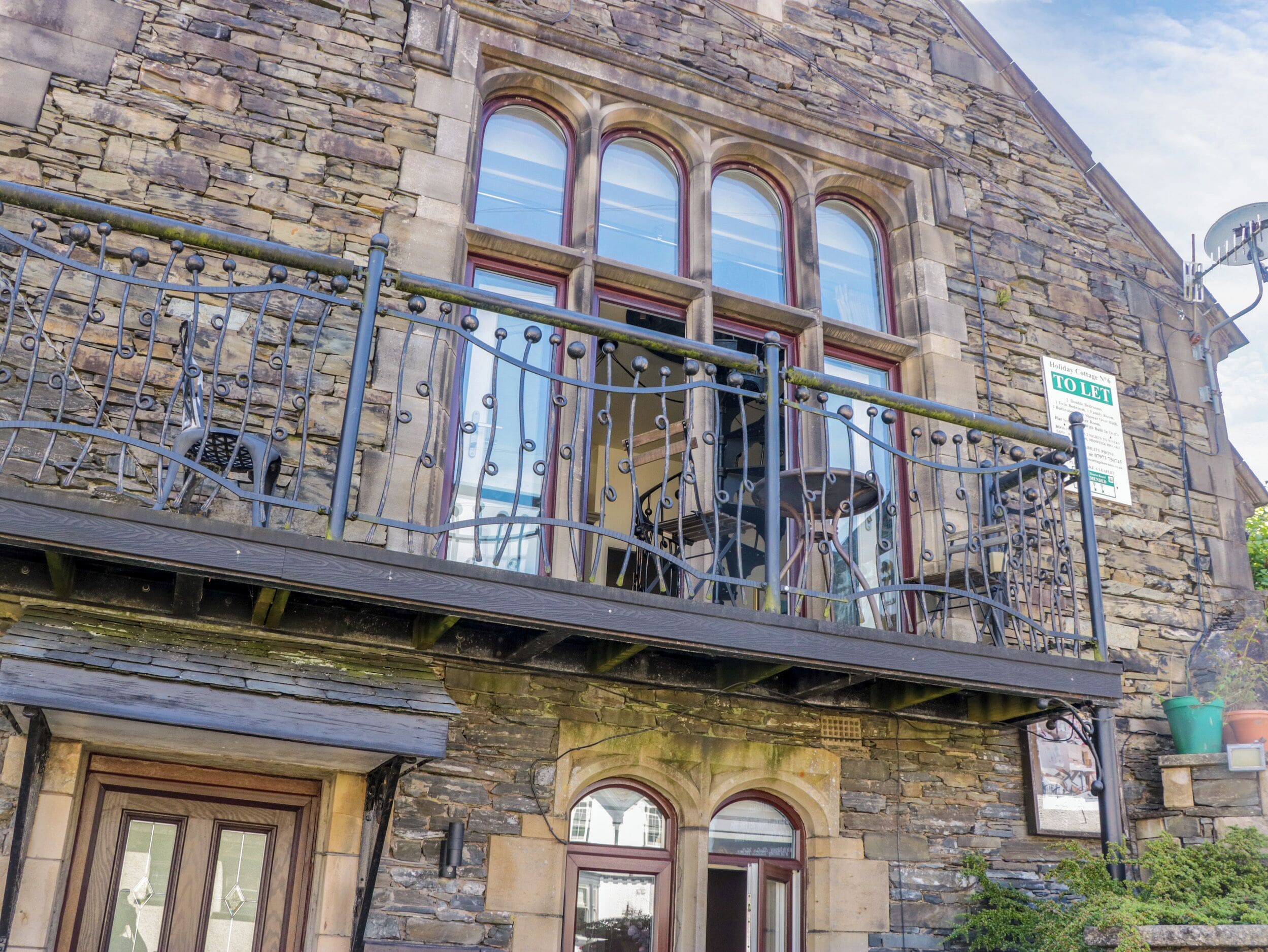A stone building with a balcony, a 'TO LET' sign, and a 'Holiday Cottage' sign.