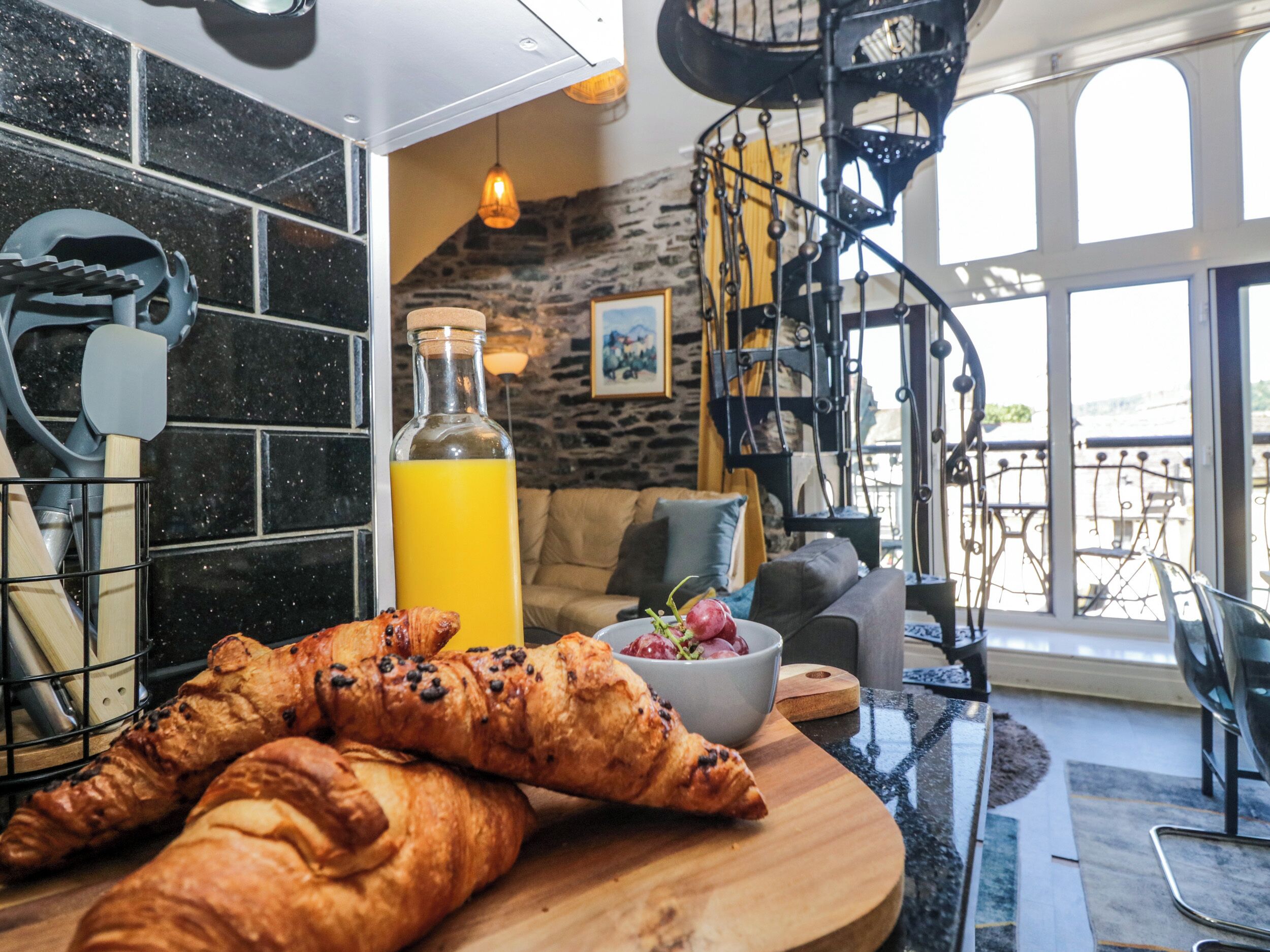 A kitchen with a wooden table, a bottle of orange juice, and croissants.