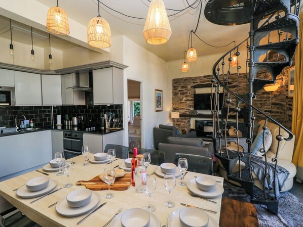 A modern kitchen with black tiled backsplash, white cabinets, and a dining area set for six with a round table. - Hillside Cottage (Windermere)