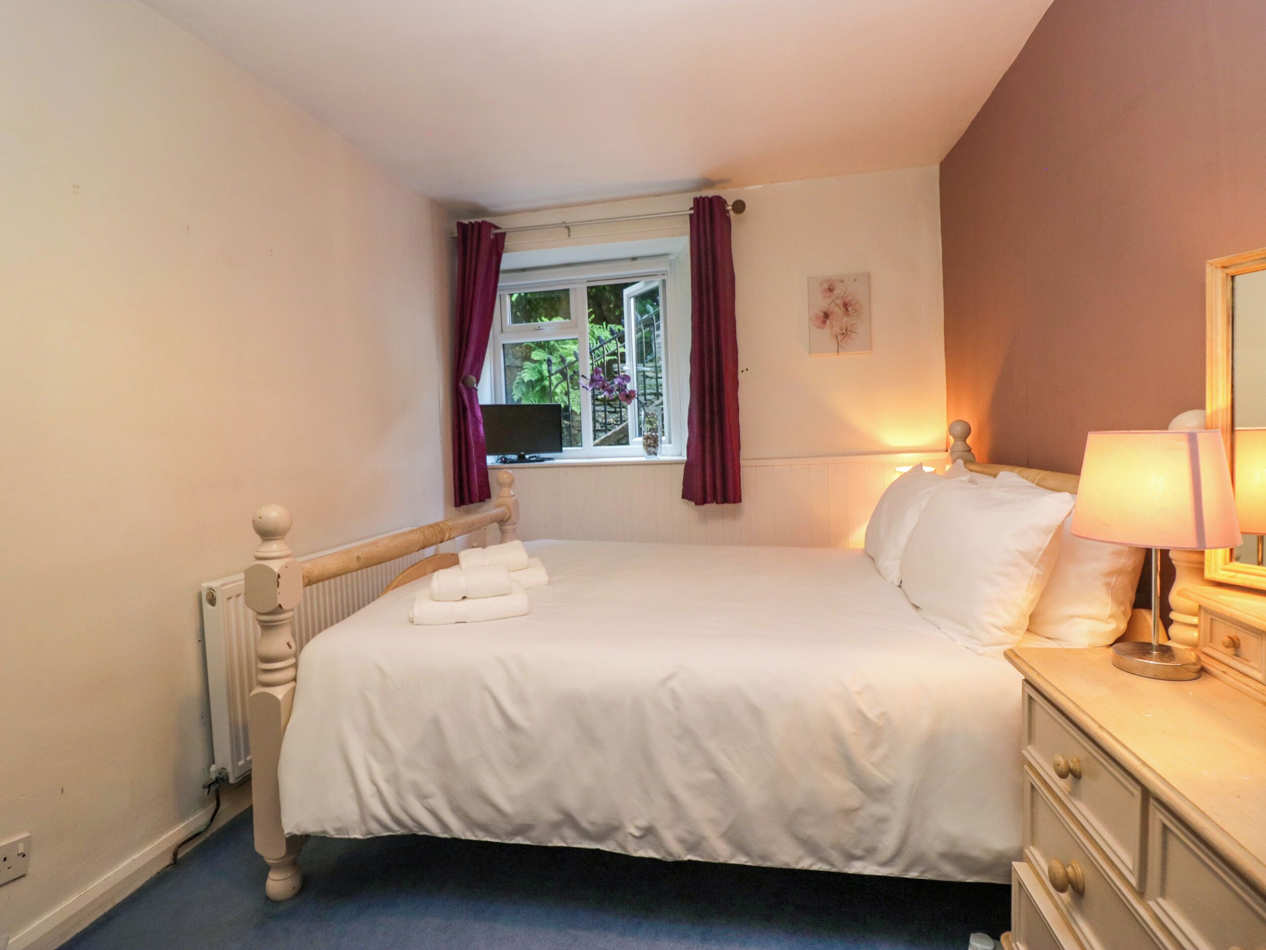 A bedroom with a bed, a dresser, a window with curtains, a radiator, and a lamp.