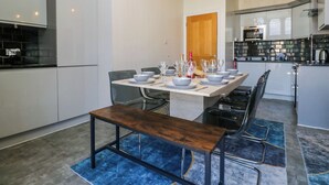 A modern kitchen with a dining area, featuring a large island, pendant lighting, and a built-in oven. - Hillside Cottage (Windermere)