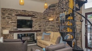 A living room with a stone wall, a fireplace, a sofa, and a staircase with a wrought iron railing. - Hillside Cottage (Windermere)