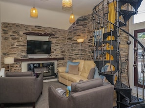 Ein Wohnzimmer mit Steinwand, Kamin, Sofa und Treppe mit schmiedeeisernem Geländer.