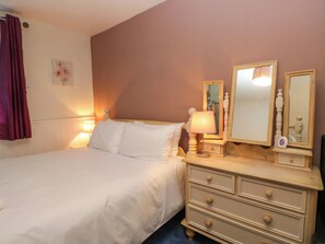 A bedroom with a bed, bedside lamps, a dresser, and a mirror. - Hillside Cottage (Windermere)