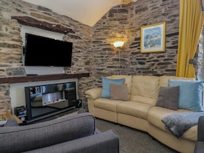 Ein Wohnzimmer mit Steinwand, einem flachbildfernseher über einem Kamin, einer Couch mit Kissen und einer Lampe.