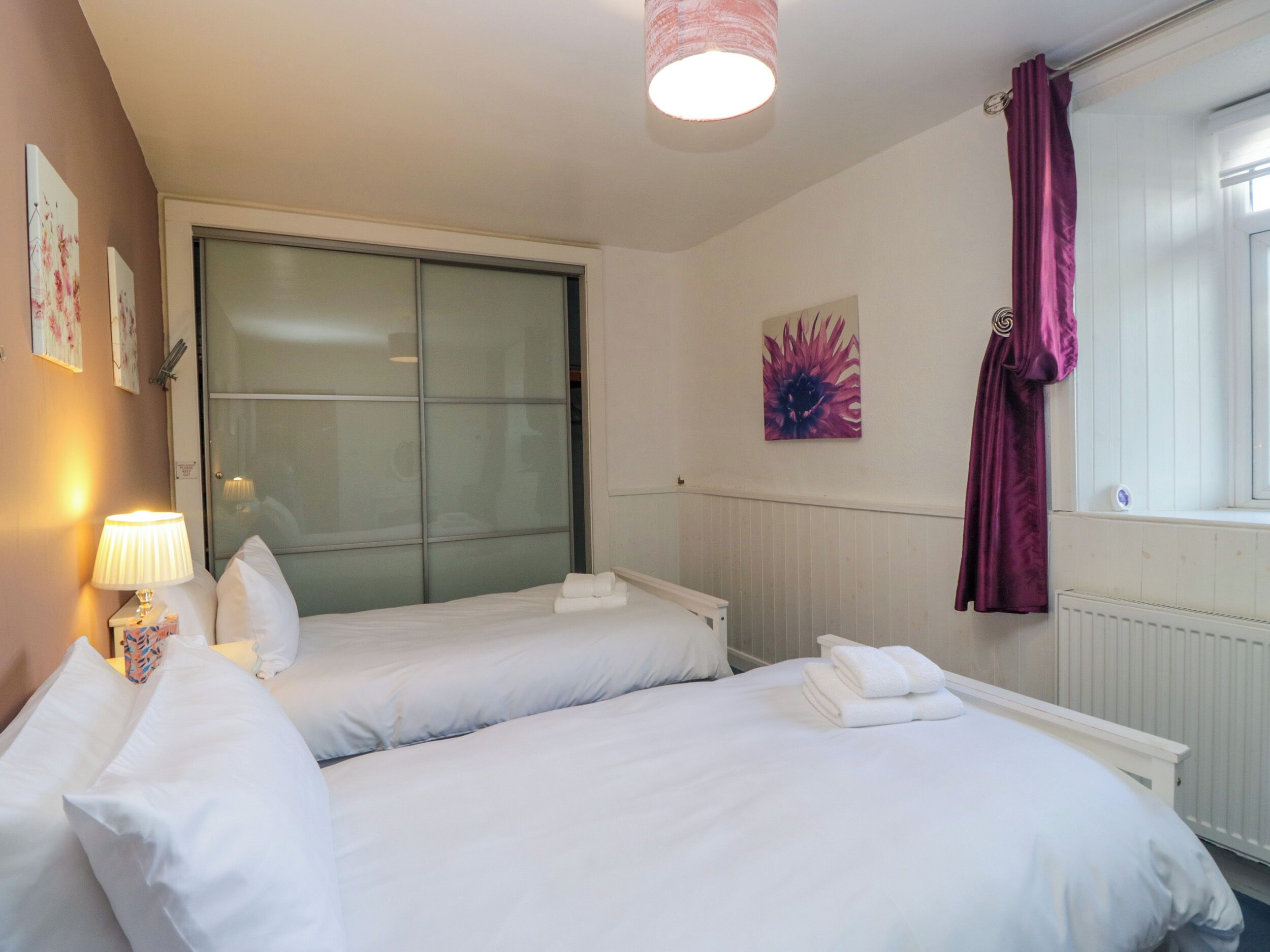 A hotel room with two beds, a window with curtains, a radiator, and a wall-mounted artwork.