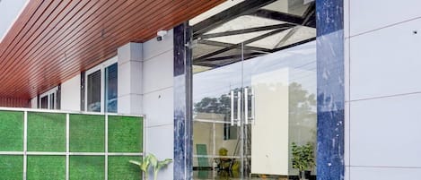 Ein moderner Gebäudeeingang mit einem Holzlamellen-Vordach, einer Glastür und einer grünen Wand mit Rasteroptik.