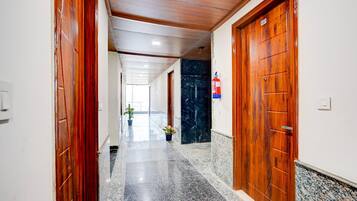 A hallway with wooden doors, a fire extinguisher, and a marble floor.