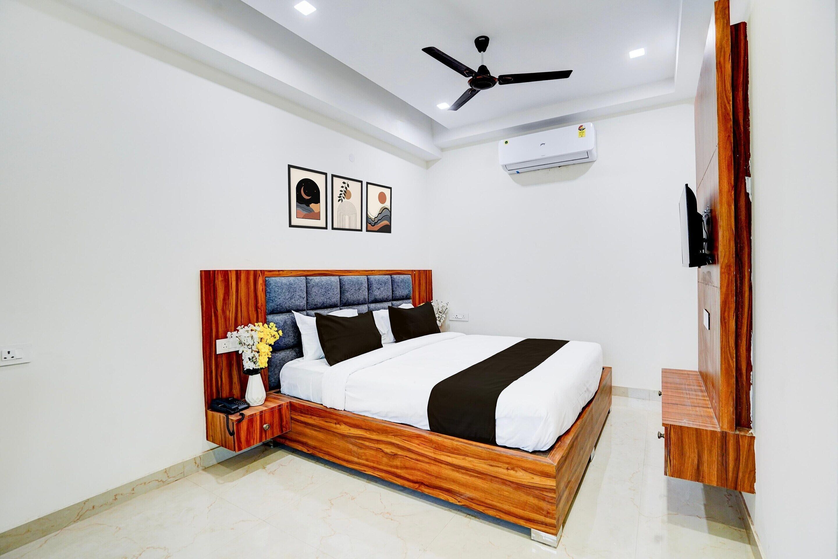A bedroom with a wooden bed frame, a ceiling fan, an air conditioning unit, and a wall-mounted TV.