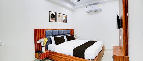 A bedroom with a wooden bed frame, a ceiling fan, an air conditioning unit, and a wall-mounted TV.