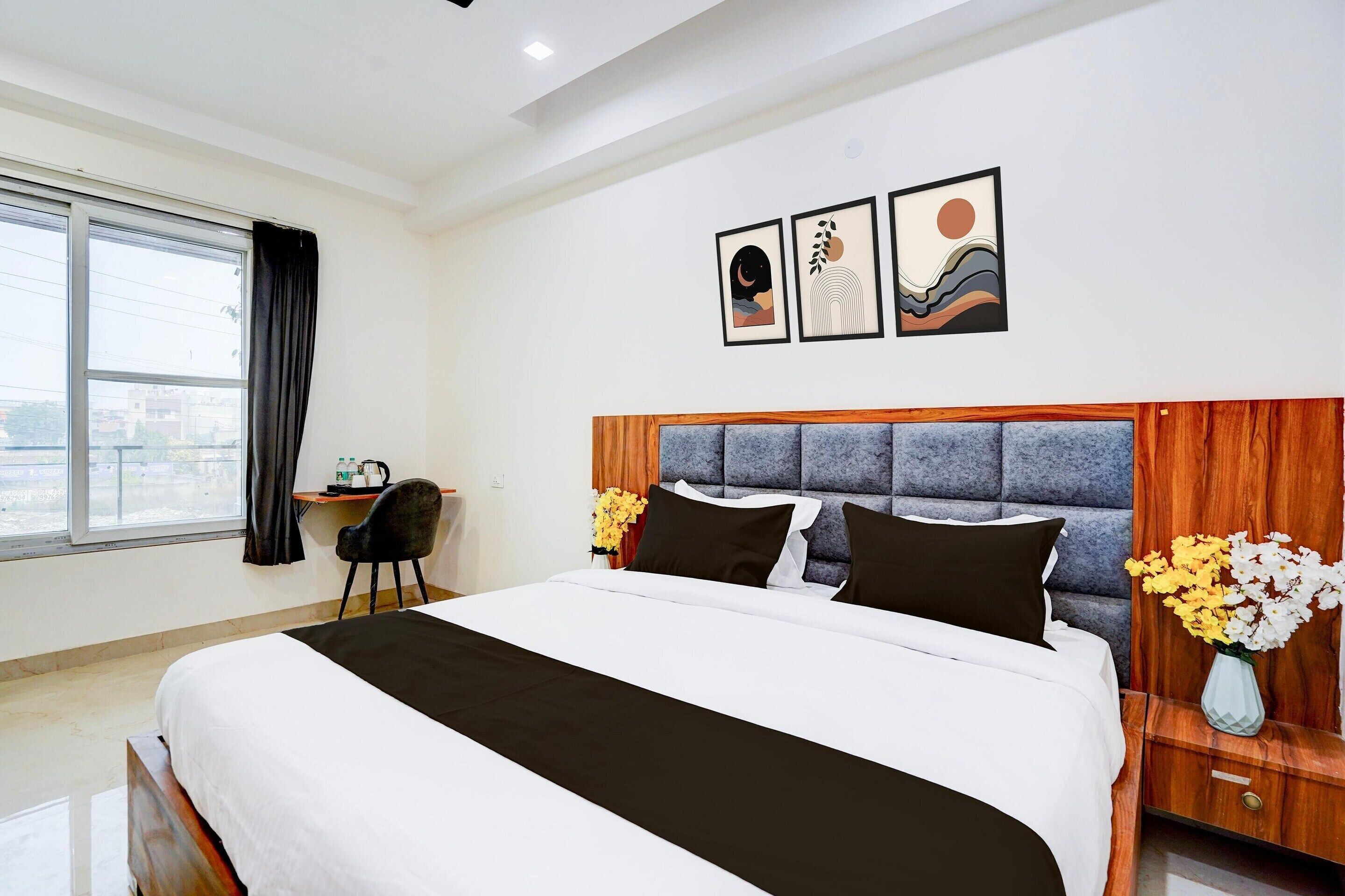 A hotel room with a large bed, a desk, a chair, a window, and artwork on the wall.