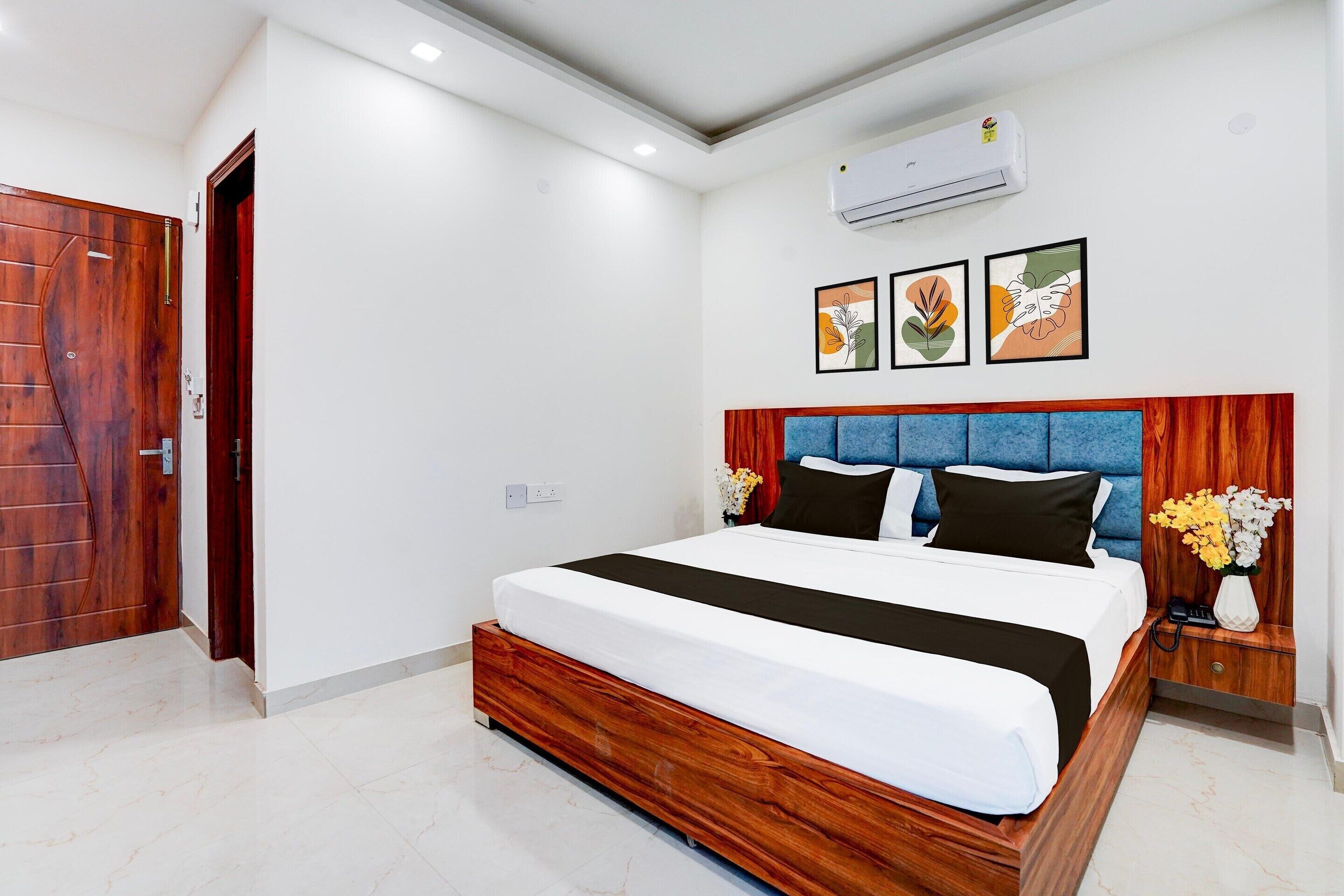 A modern hotel room with a wooden bed frame, a blue headboard, and a small bedside table with a vase of flowers.