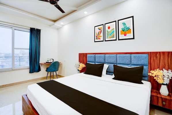 A hotel room with a large bed, a desk, a chair, and a view of the city. - Deluxe With Balcony Viva Residency (Noida)