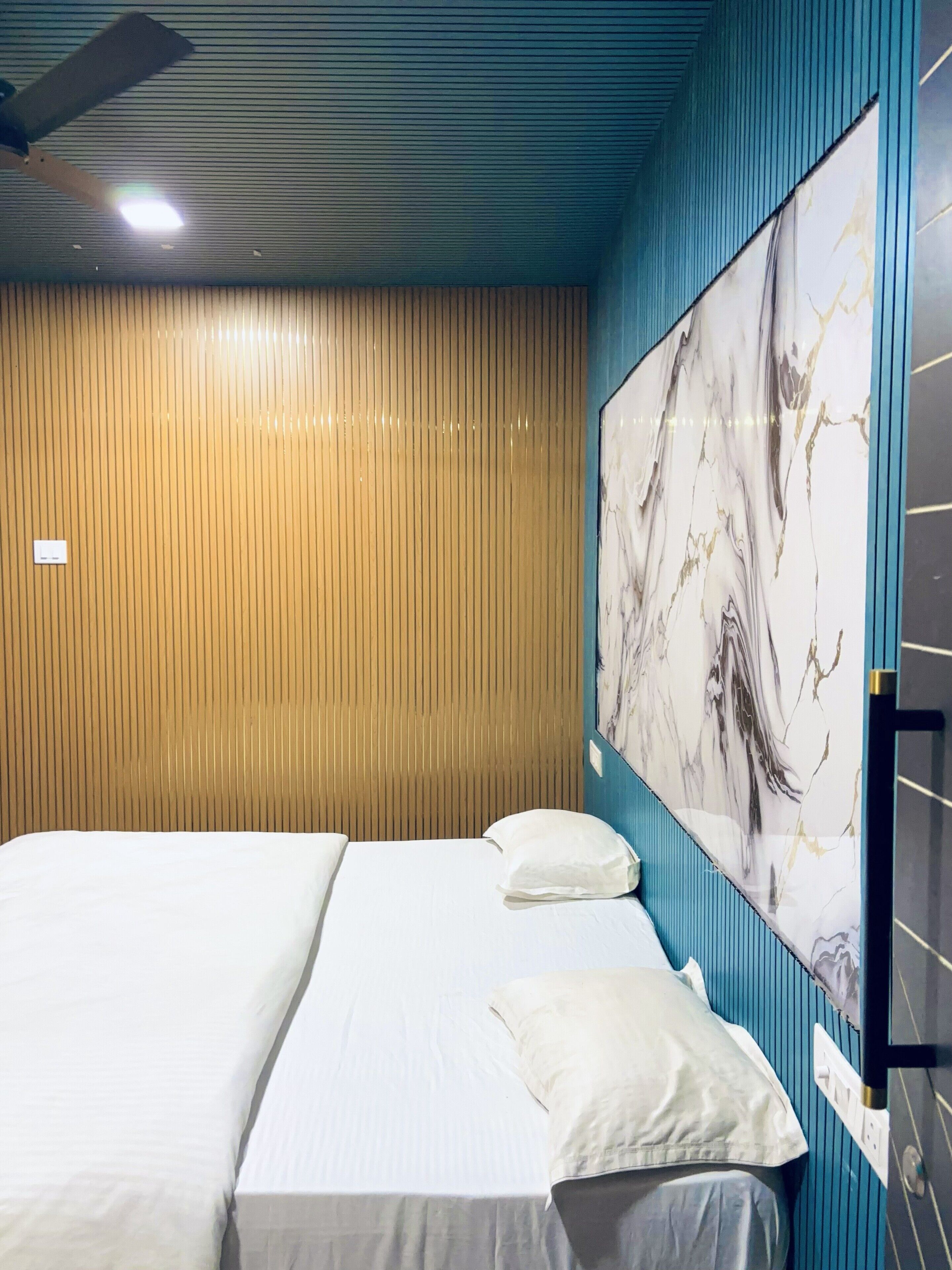 Een hotelkamer met een bed, een plafondventilator, een kunstwerk aan de muur en een wandpaneel van hout.