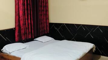A single bed with a wooden headboard, a ceiling fan, and red curtains.