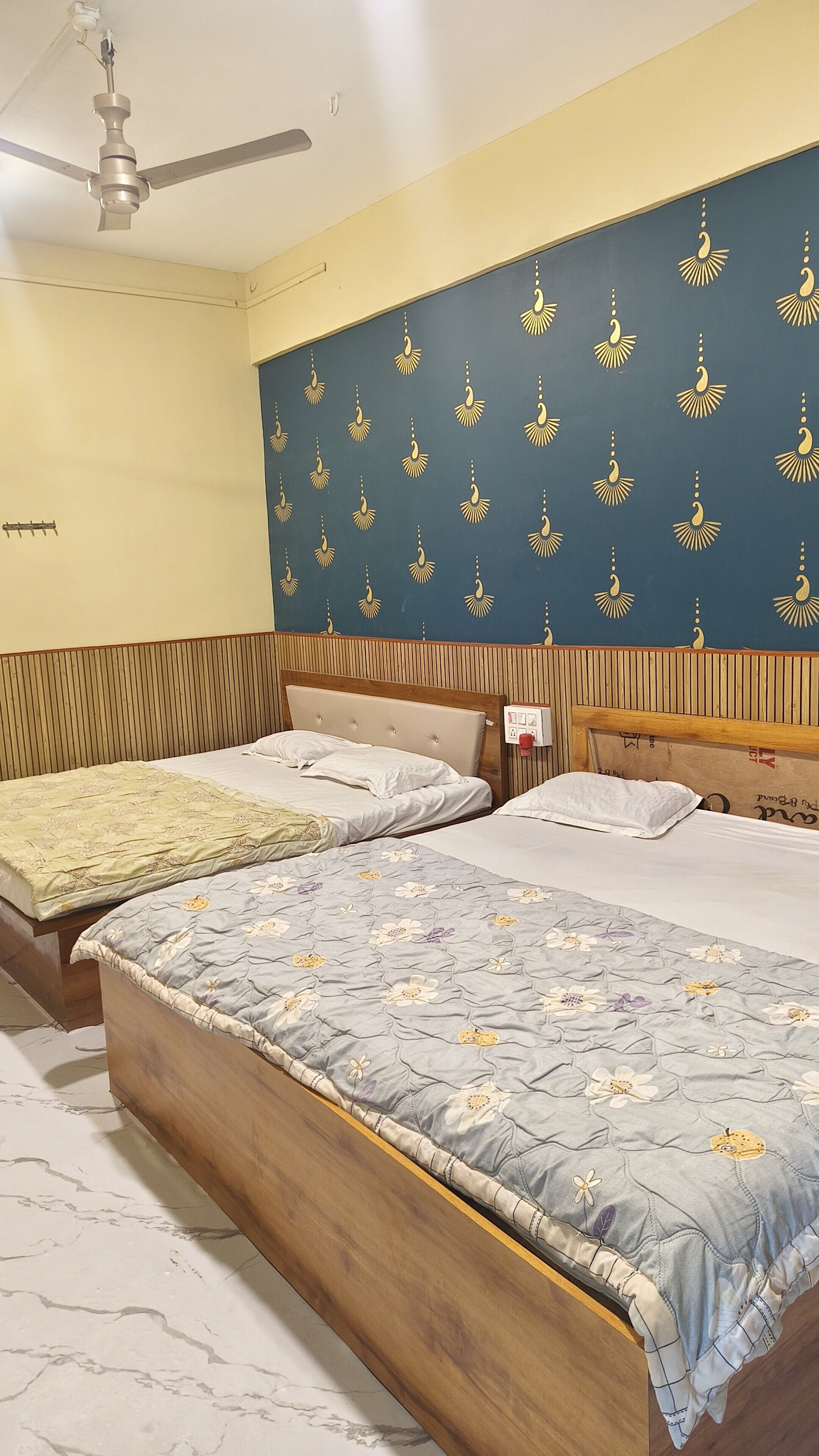 A room with two beds, a ceiling fan, and patterned wallpaper.