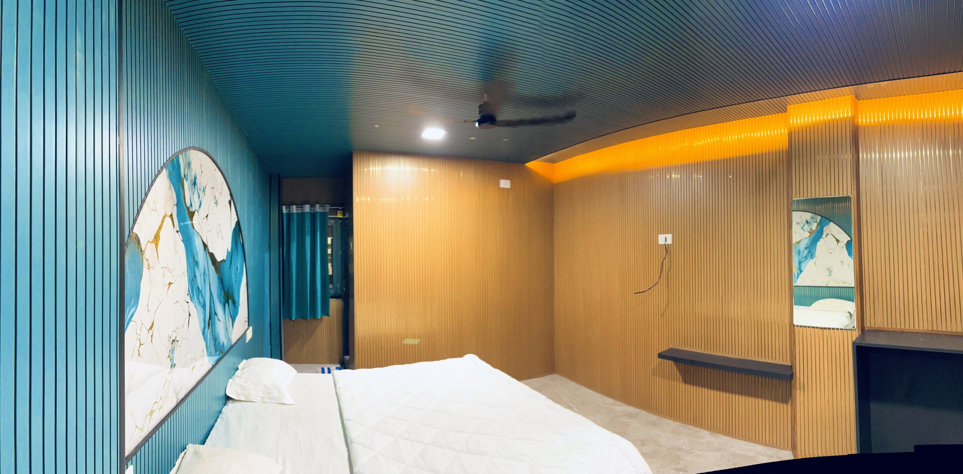 A hotel room with a bed, a wall with a decorative panel, wooden paneling, and a small shelf.