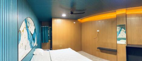 A hotel room with a bed, a wall with a decorative panel, wooden paneling, and a small shelf.