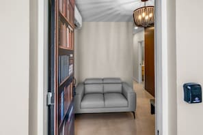 A hallway with a gray sofa, a bookshelf, a chandelier, and a door with a lock. - Casa Costa Brava | 8 Room - 16 Guest @ San Juan (San Juan de Puerto Rico)