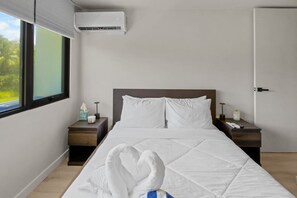 A hotel room with a bed, two bedside tables, a nightstand, a window with blinds, and an air conditioning unit. - Villa Marena | Playas del Yunque Modern Apt (Rio Grande)