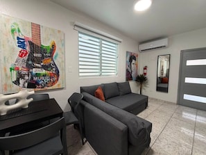 A modern living room with a grey sofa, a black dining table, and a colorful abstract painting on the wall. - Central San Juan 3BR Apt • Sleeps 8 (San Juan de Puerto Rico)