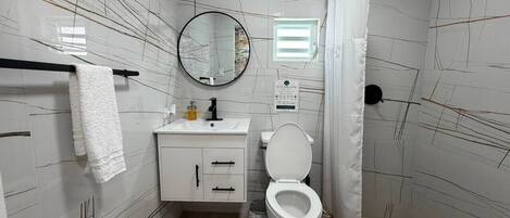 Un baño con inodoro, lavamanos, espejo y toallero.