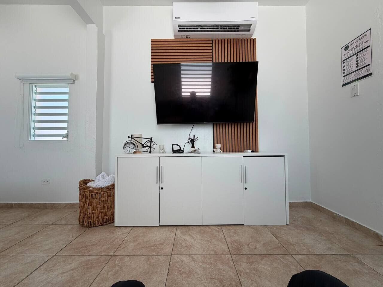 Un salon moderne avec un téléviseur à écran plat fixé au-dessus d’un meuble blanc, un panier en osier et un vélo posé sur le meuble.