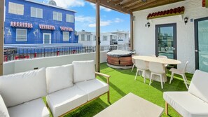 A rooftop terrace with a white sofa, a table with chairs, a hot tub, and a view of a blue building. - Costa Brava Apt 4 | Calle Loiza 3/3 Apt @ San Juan (San Juan de Puerto Rico)