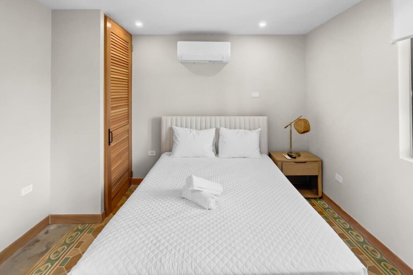 Een slaapkamer met een bed, nachtkastje, lamp en airconditioning.