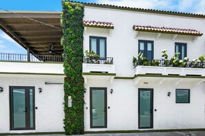 A two-story building with a white facade, green plants on the exterior, and a balcony with potted plants. - Costa Brava Apt 4 | Calle Loiza 3/3 Apt @ San Juan (San Juan de Puerto Rico)