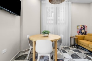 A room with a round wooden table, white chairs, a small potted plant, a yellow sofa, and a painting on the wall. - Costa Brava Apt 1 | Calle Loiza Cozy @ San Juan (San Juan de Puerto Rico)