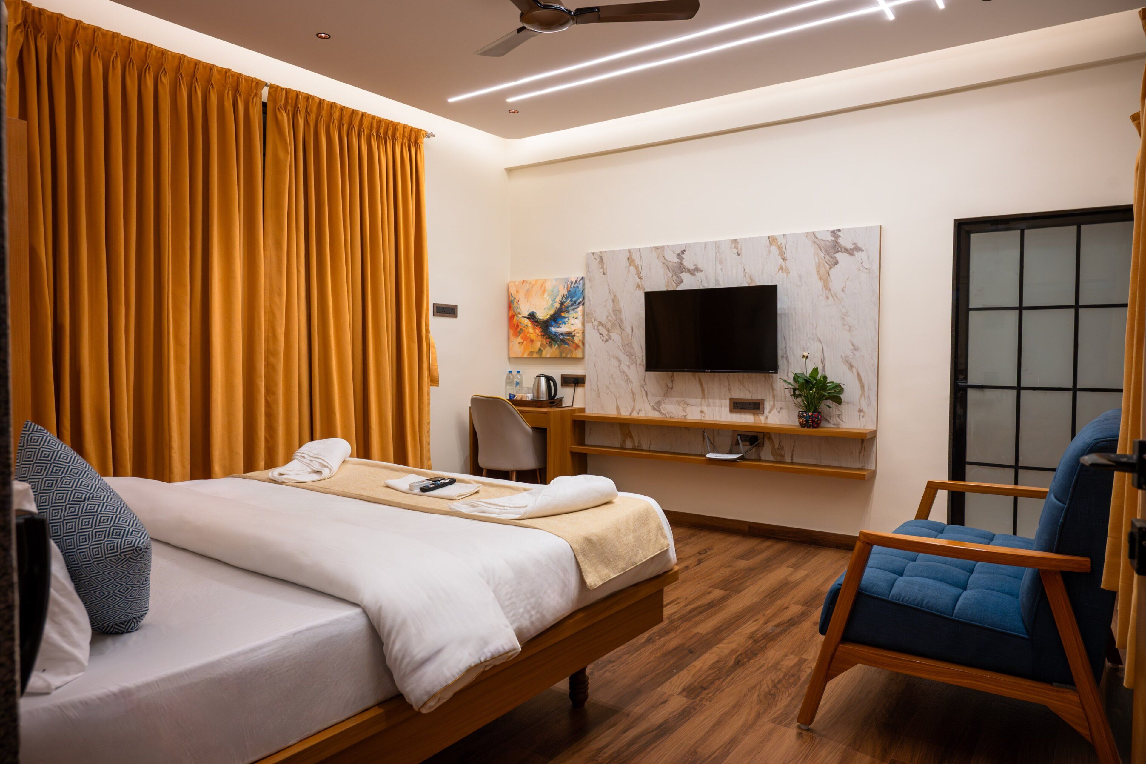 A hotel room with a bed, a desk, a chair, a TV mounted on the wall, and a window with curtains.