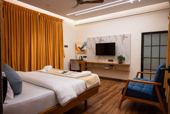 A hotel room with a bed, a desk, a chair, a TV mounted on the wall, and a window with curtains.