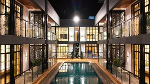 A hotel interior with a central pool, multiple rooms with large windows, and a traditional Asian-style gate.