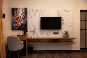 A modern living room with a mounted TV, a wooden entertainment unit, a grey chair, and a painting of a violin.