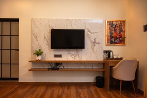 A modern room with a flat-screen TV mounted on a marble wall, a wooden desk with a chair, a potted plant, and a painting.