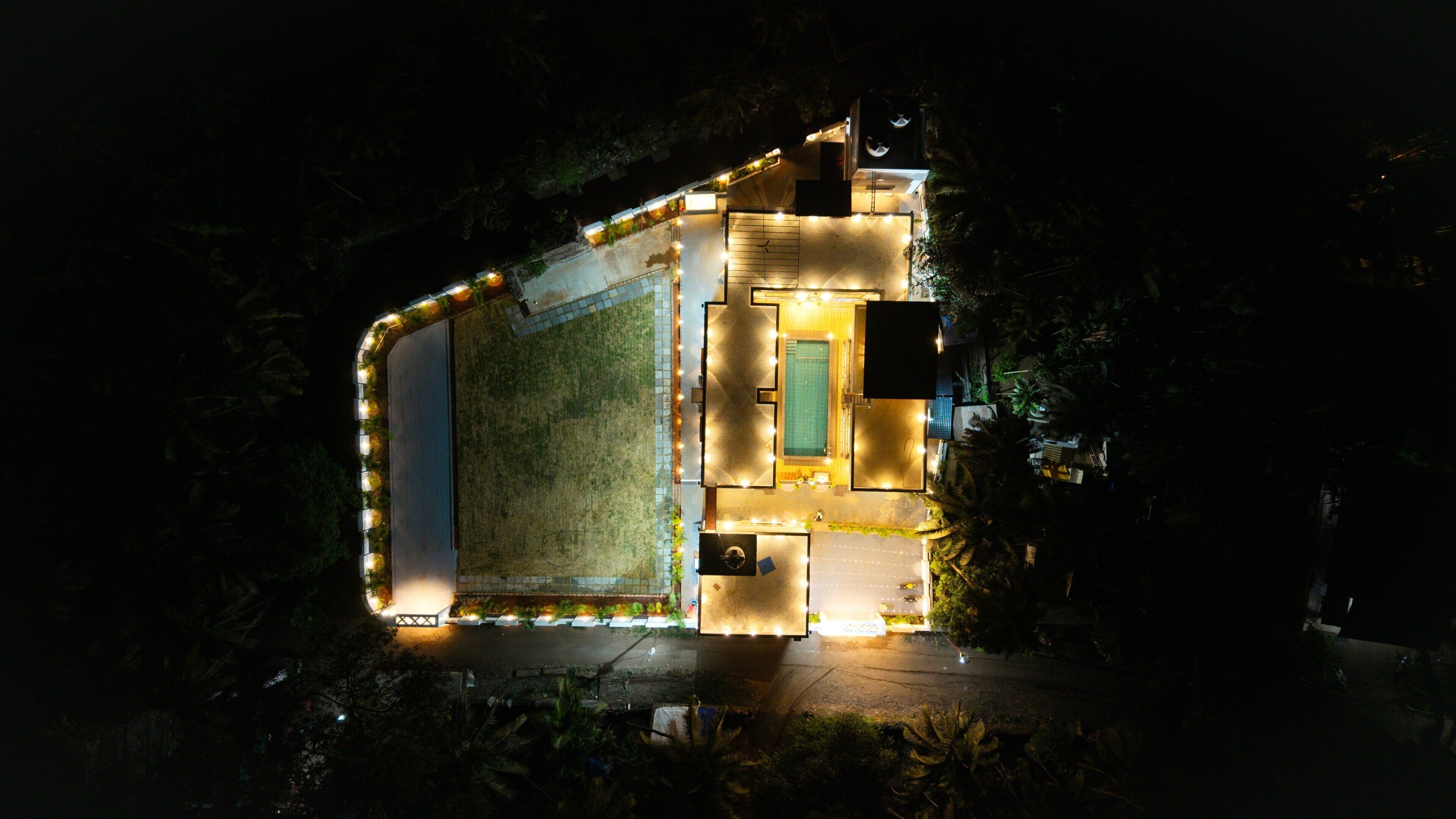 An aerial view of a hotel with a swimming pool, a tennis court, and a well-lit perimeter.