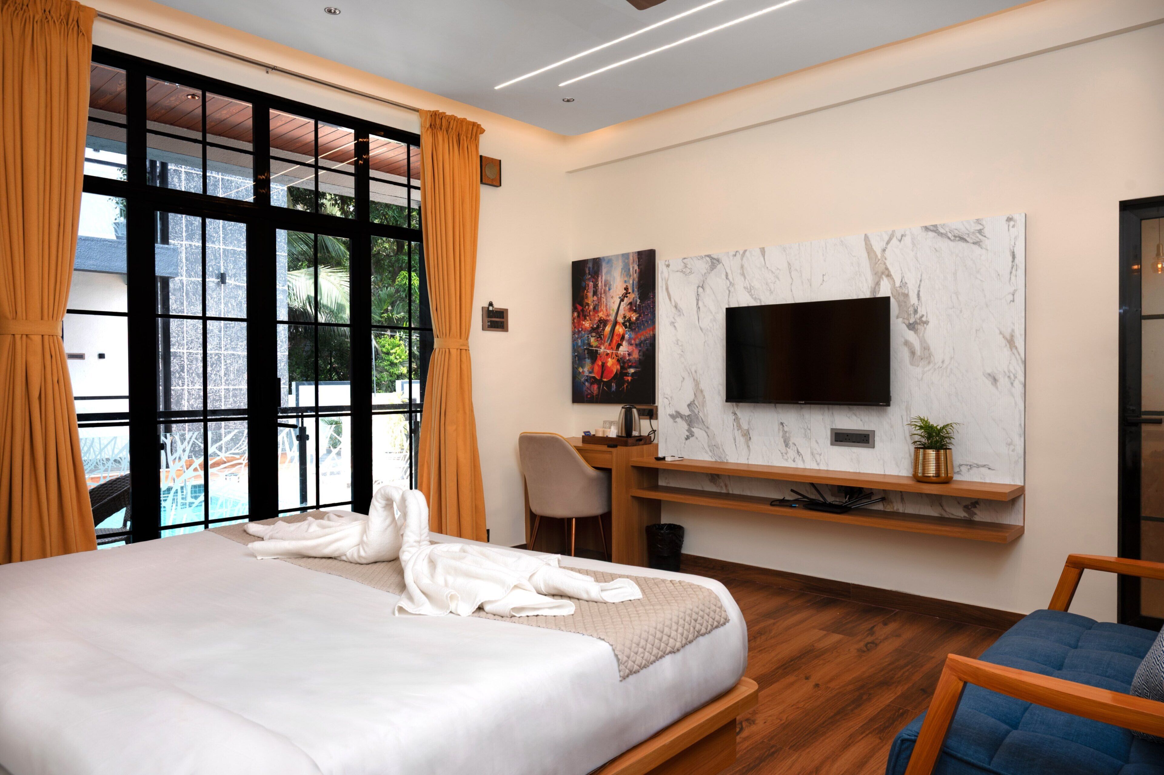 Habitación de hotel moderna con una cama grande, un escritorio, un televisor de pantalla plana montado en una pared de mármol y vistas al exterior a través de amplias ventanas.