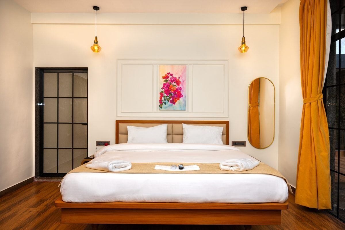 Una habitación de hotel con cama, un cuadro, un espejo y una ventana con cortinas.