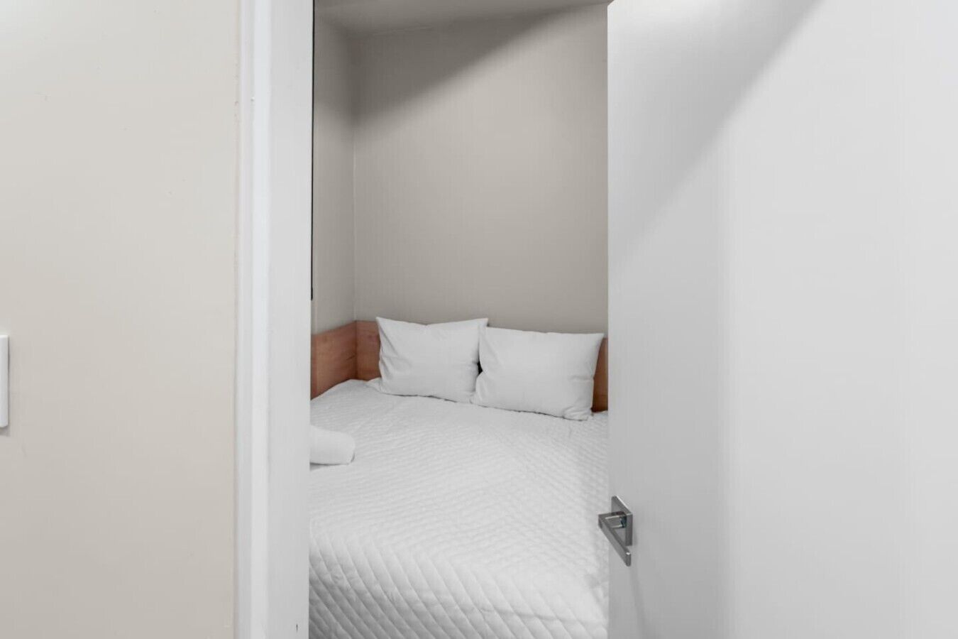 A small, neatly arranged bedroom with a single bed, white bedding, and a wooden headboard.