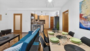 Un espace repas moderne avec une longue table, des bancs recouverts d’un tissu bleu et une cuisine en arrière-plan.