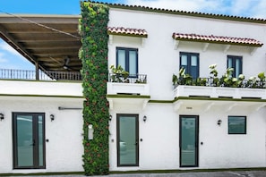 A two-story building with a white facade, green plants on the exterior, and a balcony with potted plants. - Costa Brava Apt 3 | Calle Loiza 1/1 @ San Juan (San Juan de Puerto Rico)
