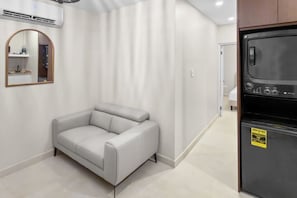 A modern living room with a grey sofa, a large mirror, and a black refrigerator. - Costa Brava Apt 3 | Calle Loiza 1/1 @ San Juan (San Juan de Puerto Rico)